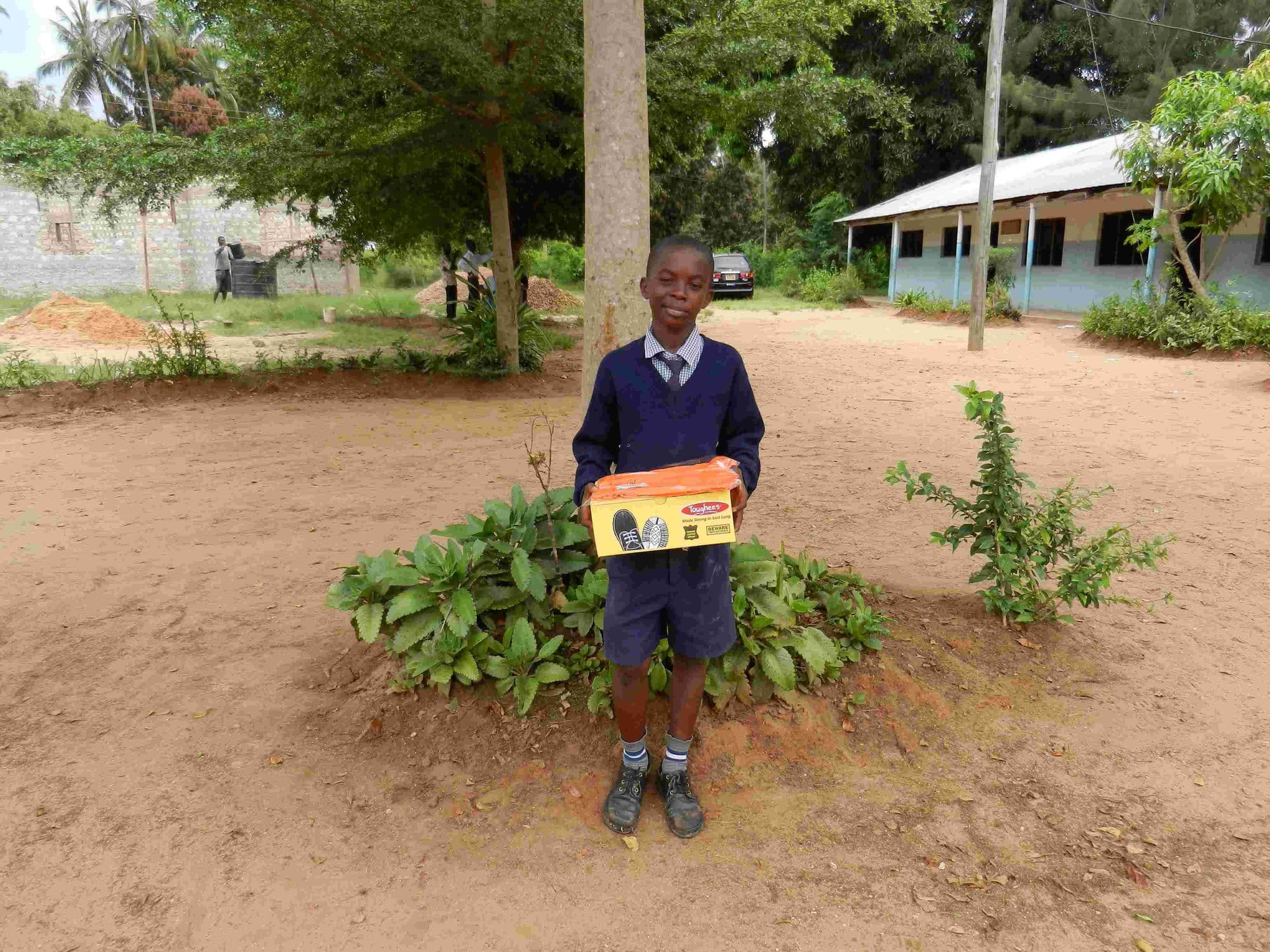 A pupil in uniform holding a shoebox outside the school