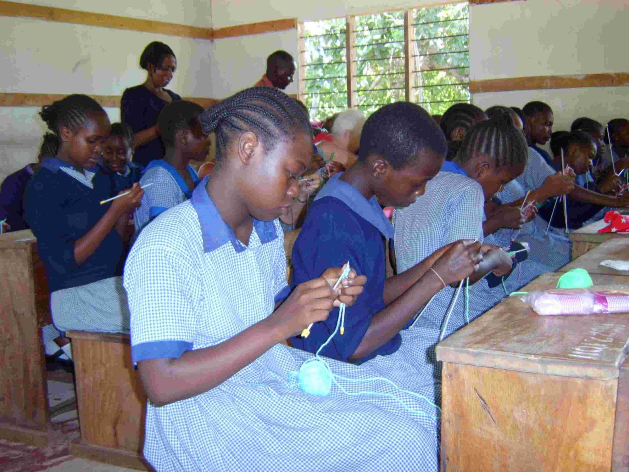 Schoolgirls knitting at their desks in a classroom