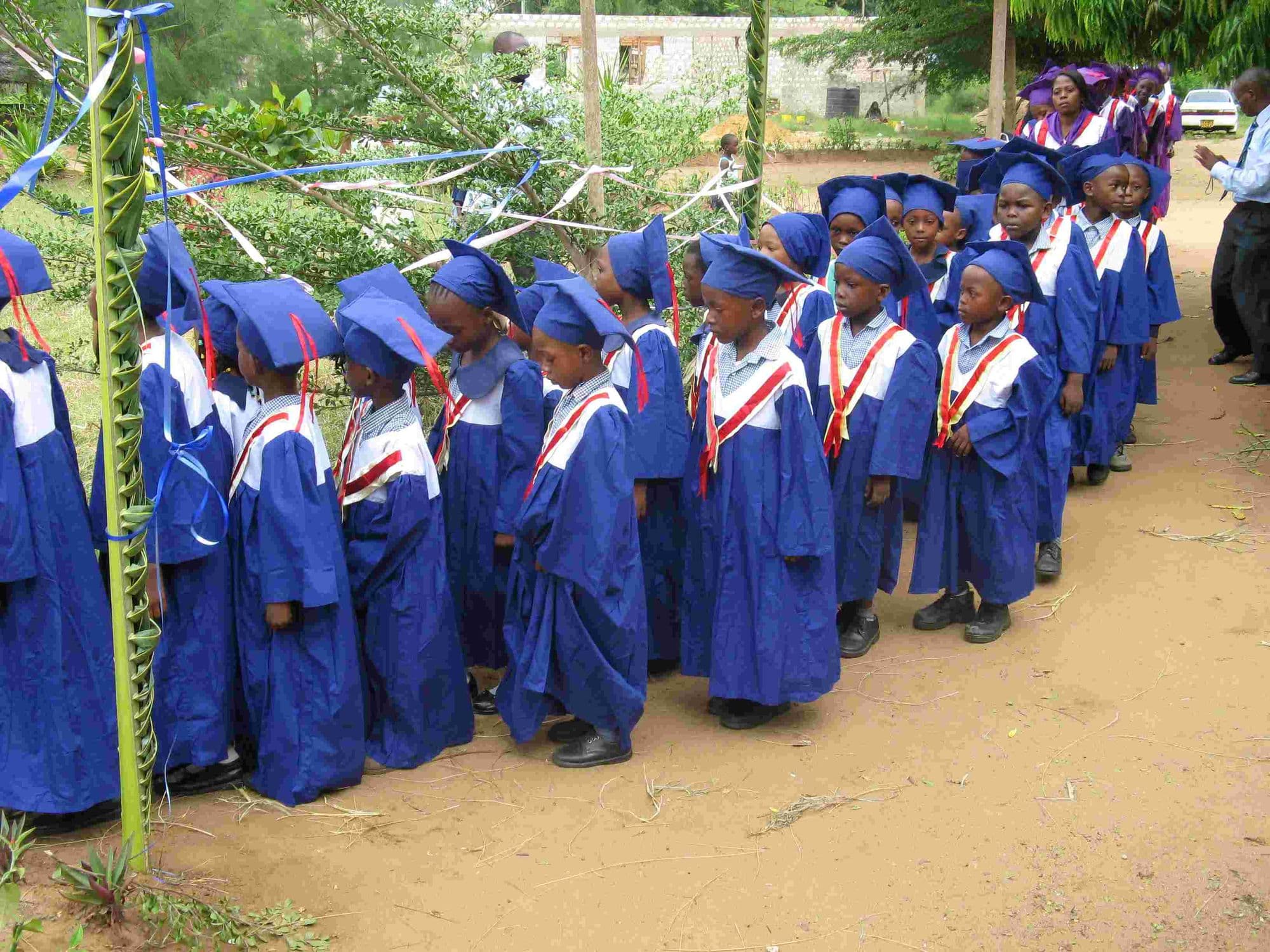 A line of nursery graduates in blue gowns and mortarboards walking under decorations