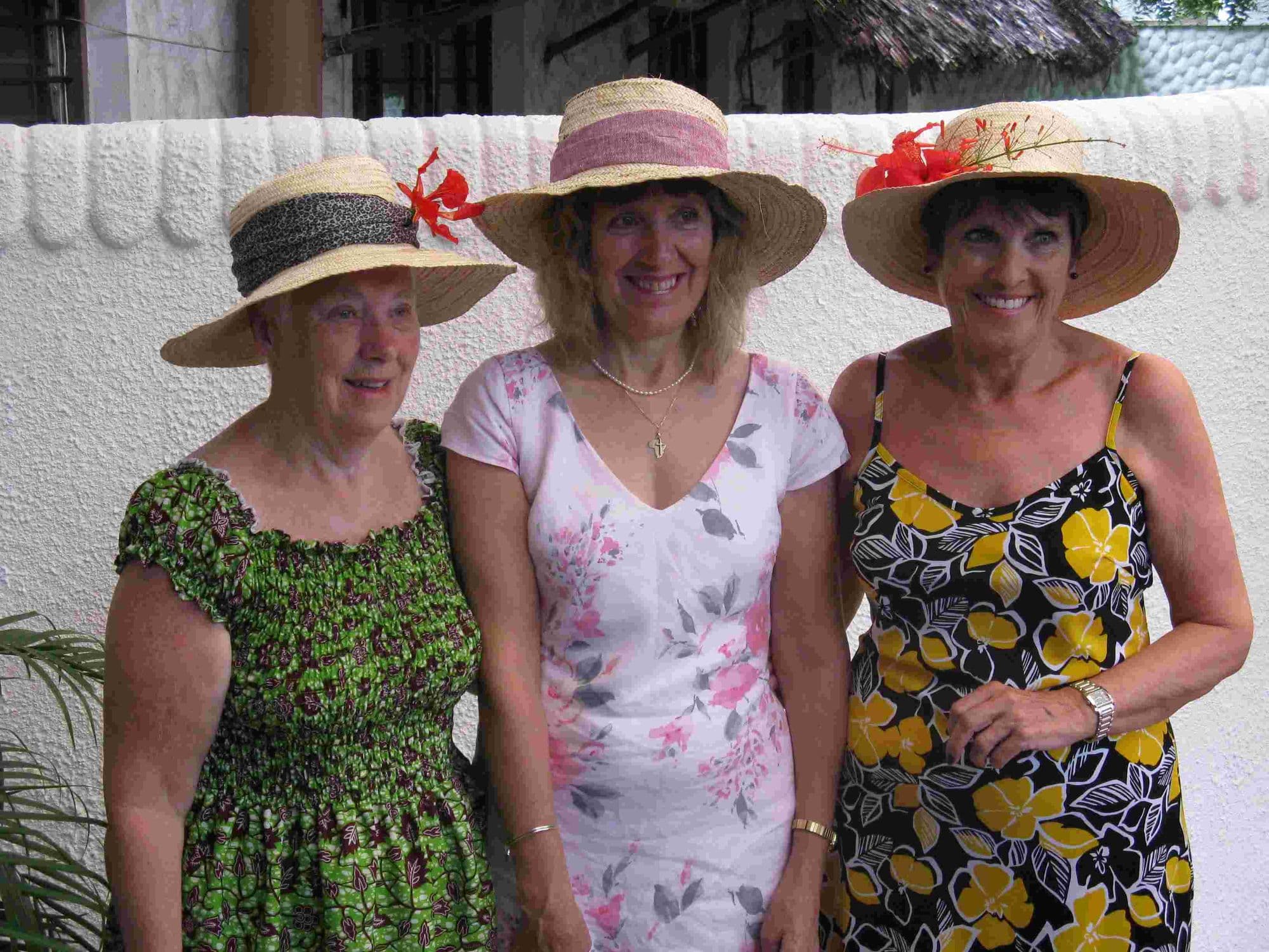 Three visiting women in sun hats and summer dresses smiling together