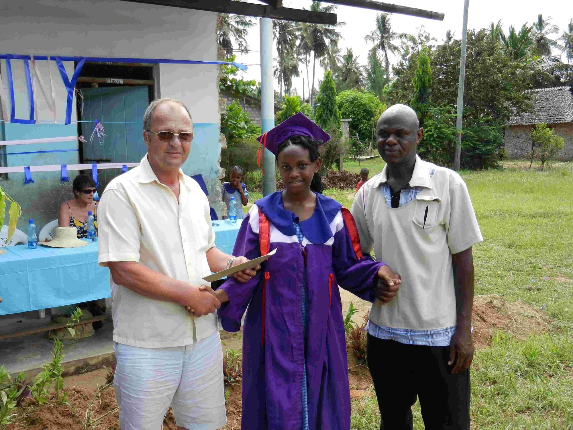 A visitor handing a gift to a graduate in a purple gown beside a teacher