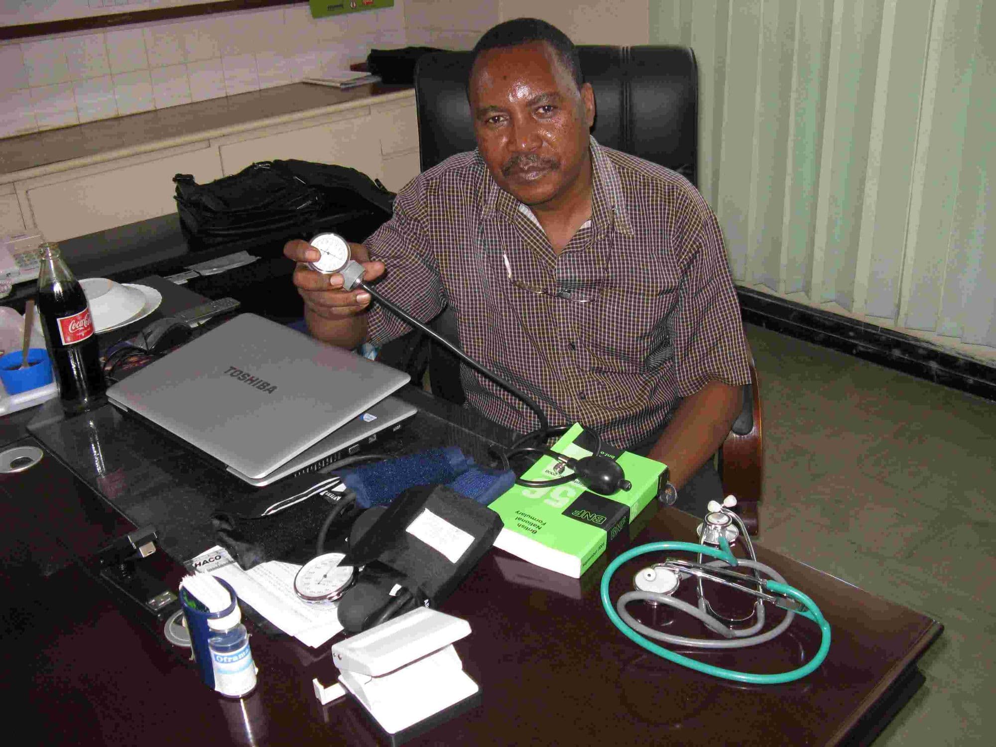 A doctor at his desk with donated stethoscopes and blood pressure monitors