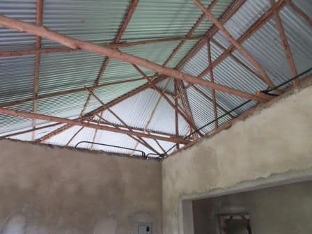 Timber roof trusses under corrugated iron sheets inside a room with freshly plastered walls