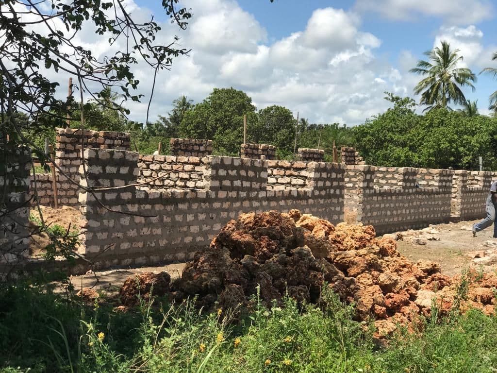 Walls of a coral-block building rising to window height, behind a heap of red coral stone