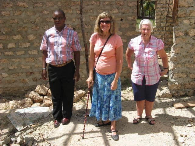 Three people standing in front of an unfinished coral-stone wall