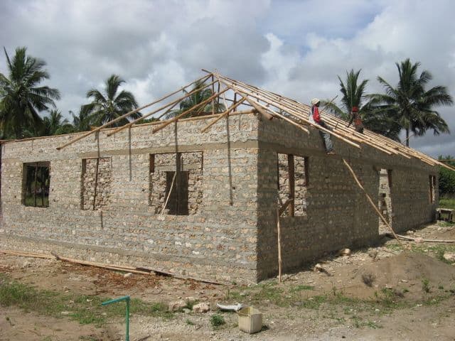Coral-block building with window openings as workers fit roof timbers