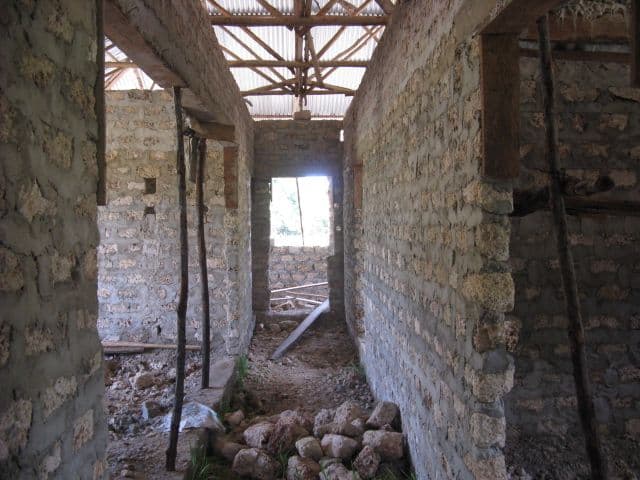 Unplastered corridor between coral-block rooms, looking towards a window, with roof timbers above