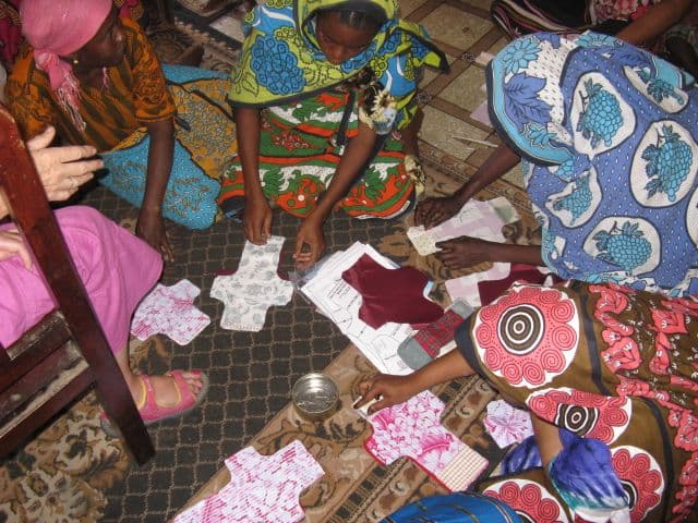 Women kneeling on a mat laying out paper patterns and cut fabric shield shapes