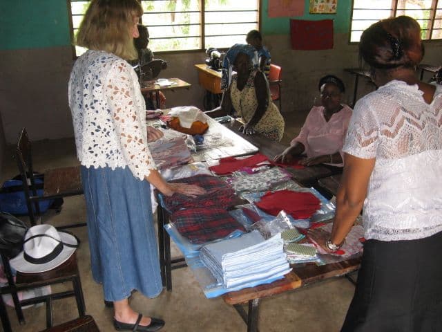 A volunteer and a woman sorting piles of fabric at a classroom table as others sew behind