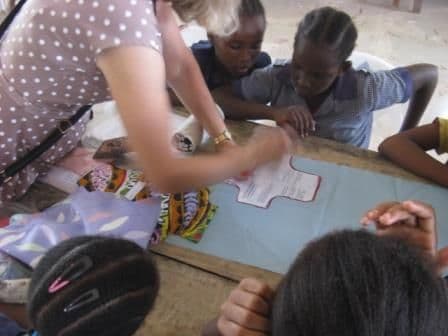 A volunteer shows schoolgirls how to cut a shield shape from waterproof fabric on a template