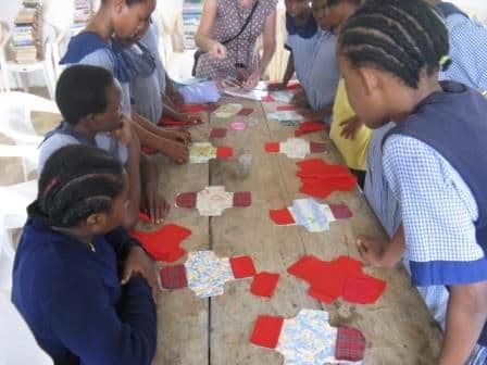 Schoolgirls around a long table laying out red and patterned fabric shield pieces