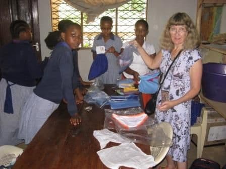 A volunteer and schoolgirls packing pants and fabric items into drawstring bags at a table
