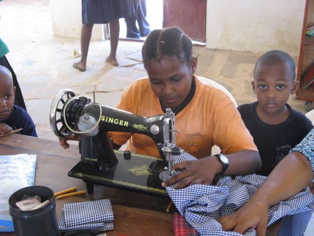 A girl in an orange T-shirt sewing checked fabric on a Singer sewing machine as a boy watches